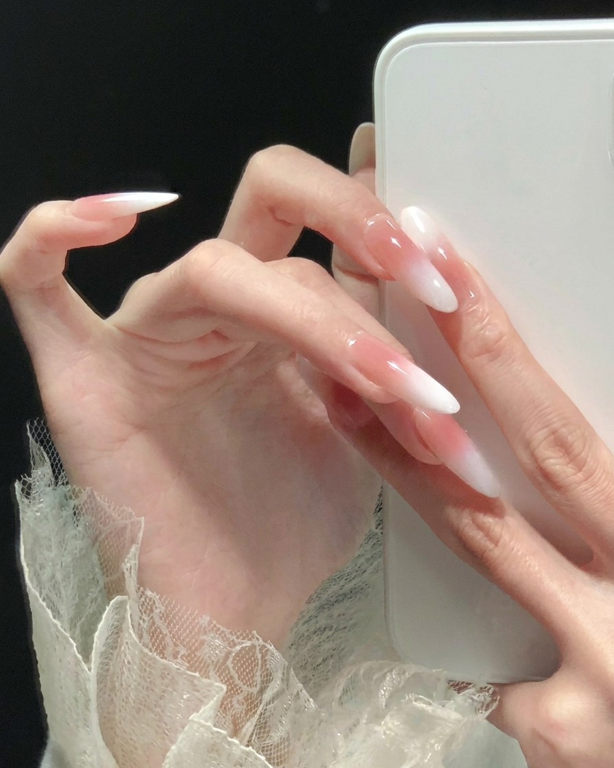 A side profile view of long, almond-shaped nails with a pink and white ombre finish.