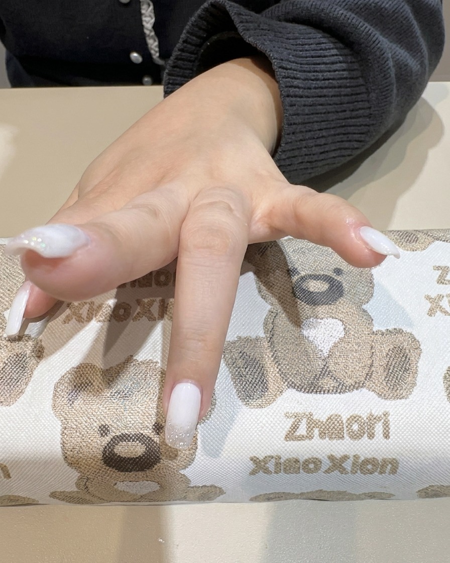A hand inside a UV lamp curing the newly applied white gradient nails.