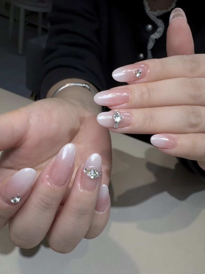 Elegant almond-shaped nails featuring a soft white-to-nude ombre gradient, pearlescent aurora chrome finish, and large silver rhinestone accents on the ring fingers.