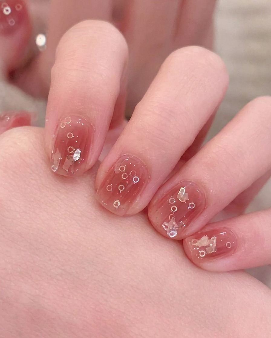 A brush applying a thin layer of pink magnetic gel polish onto a nail.