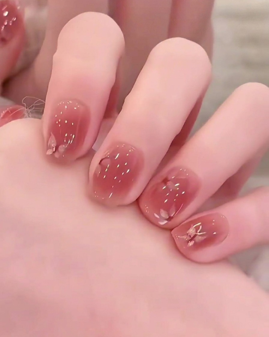A small magnetic wand being held over a wet pink gel nail to form a glowing shimmer line.