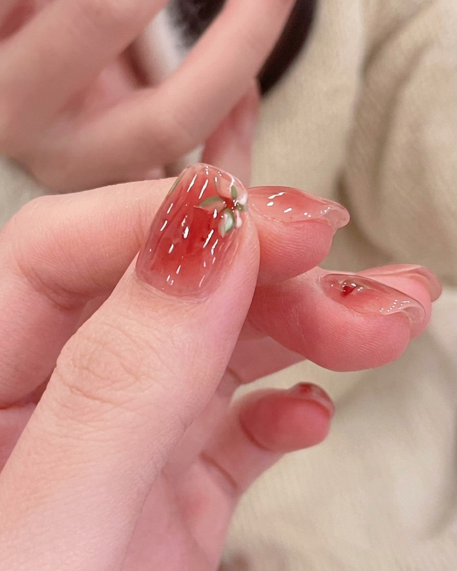 Close-up of a hand using a detail brush to add shading to the center of a hand-painted pink magnolia on a nail.