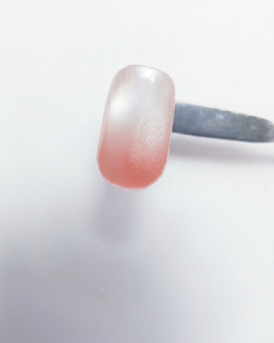A close-up view of a gel brush depositing peach-pink gel onto the tip of a nail that already has a milky white base.