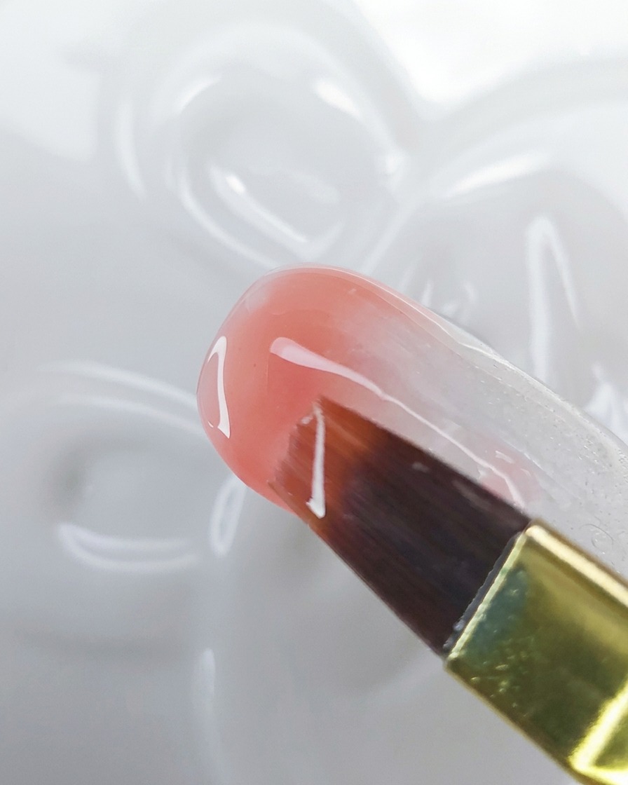 A close-up of a brush dragging peach-pink gel upward over a milky white base to create an ombre effect.