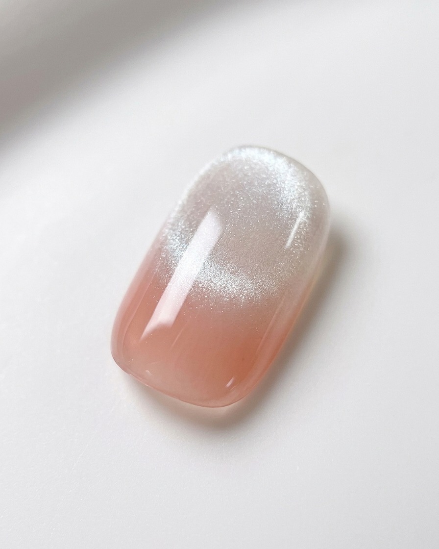 A spherical nail magnet being held steady over a pink and white gradient nail with wet magnetic gel, highlighting the formation of a bright cat-eye streak.