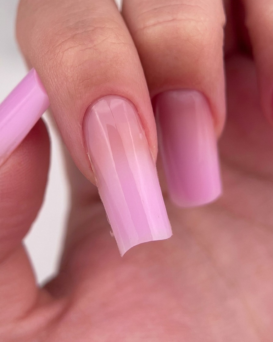 A close-up of a finger with a clear, glossy base coat applied to the nail.