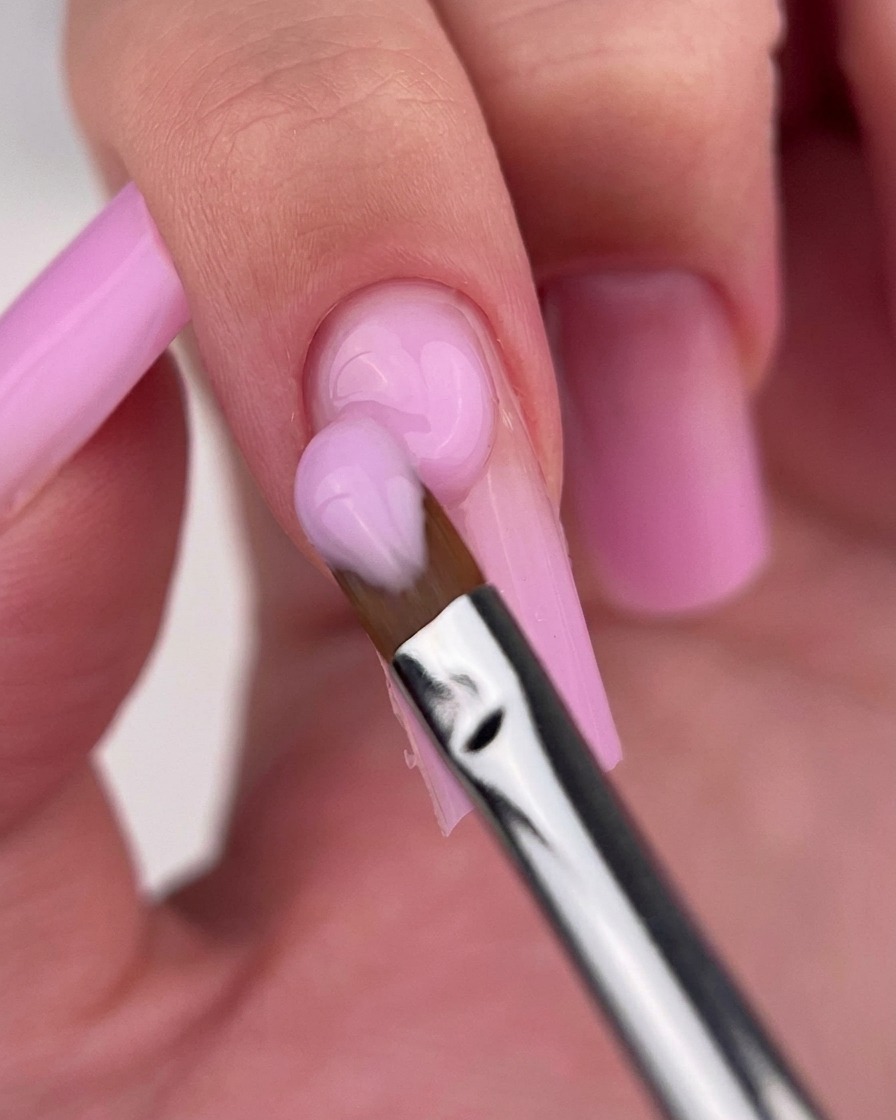 A clean gel brush gently blending the junction of two pink polish shades on a nail.