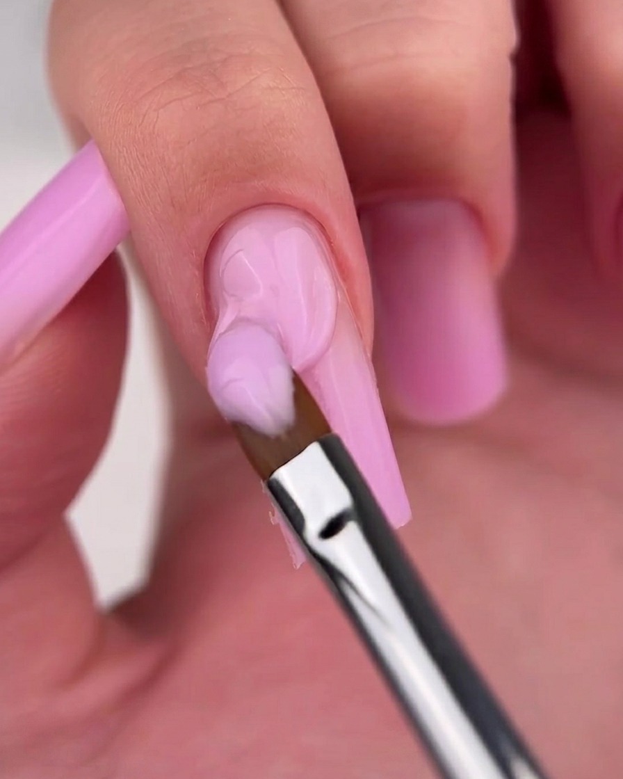 Close-up of a brush smoothing the gradient transition on a pink ombre nail.