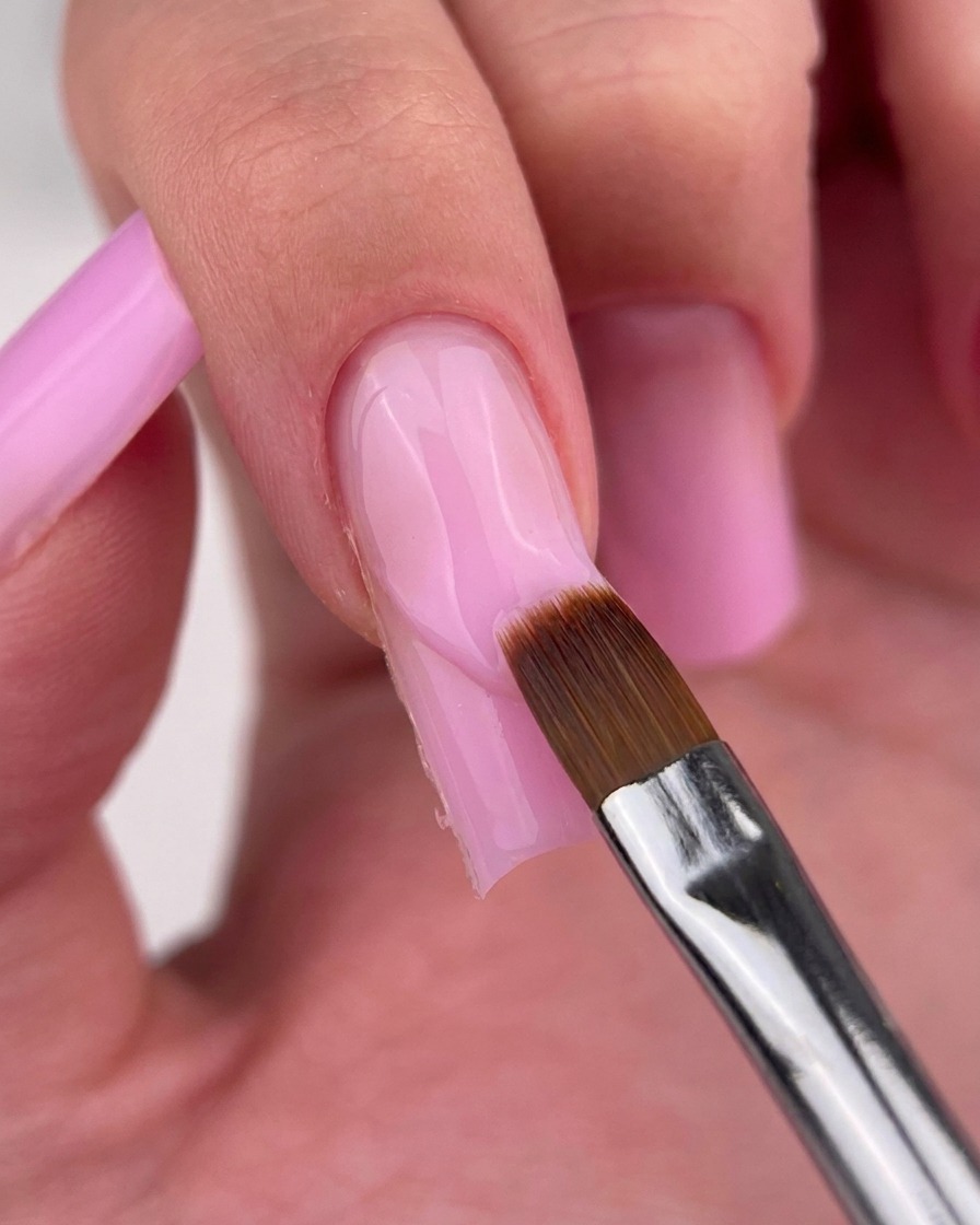 A fine liner brush carefully cleaning up the edge of the pink gel at the cuticle.