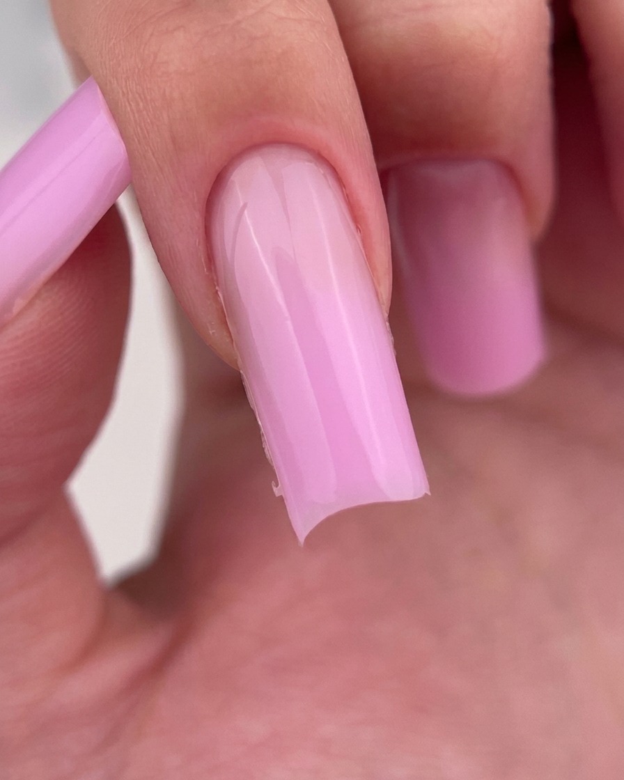 A close-up view of a nail file refining the free edge of a square-shaped, light pink gel-coated nail.