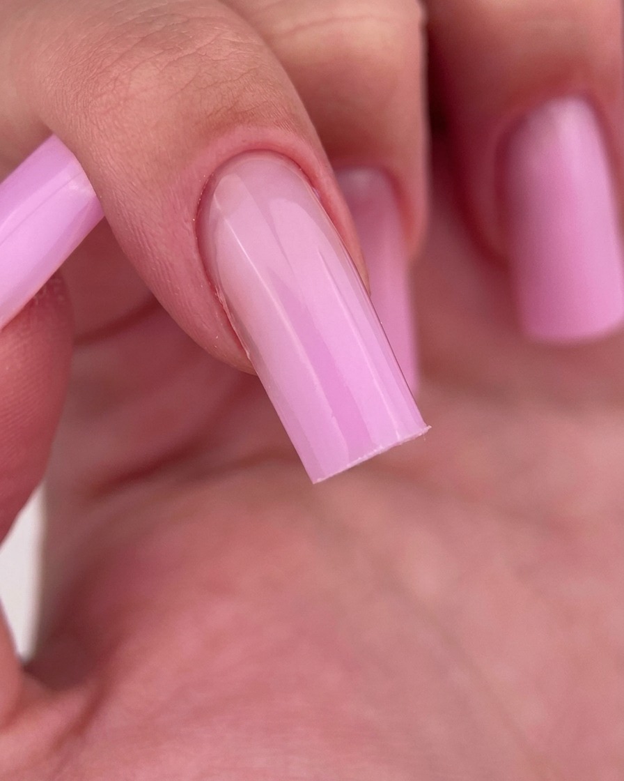 A close-up of a finger being wiped clean with a lint-free pad, revealing the glossy pink gel finish.