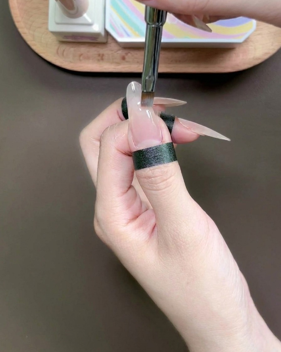 A specialized dabbing tool placing a drop of blue gel onto the tip of a fingernail.