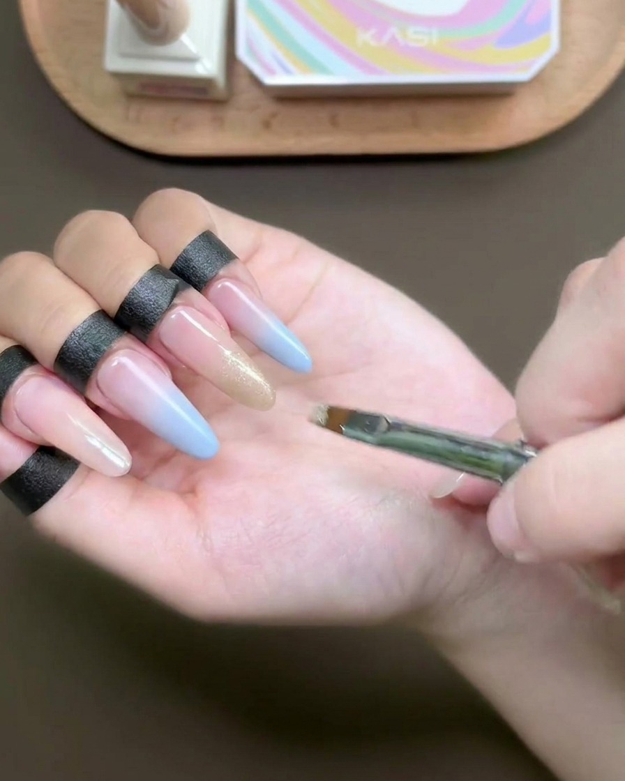 A flat brush applying shimmering champagne cat-eye gel to a fingernail tip.
