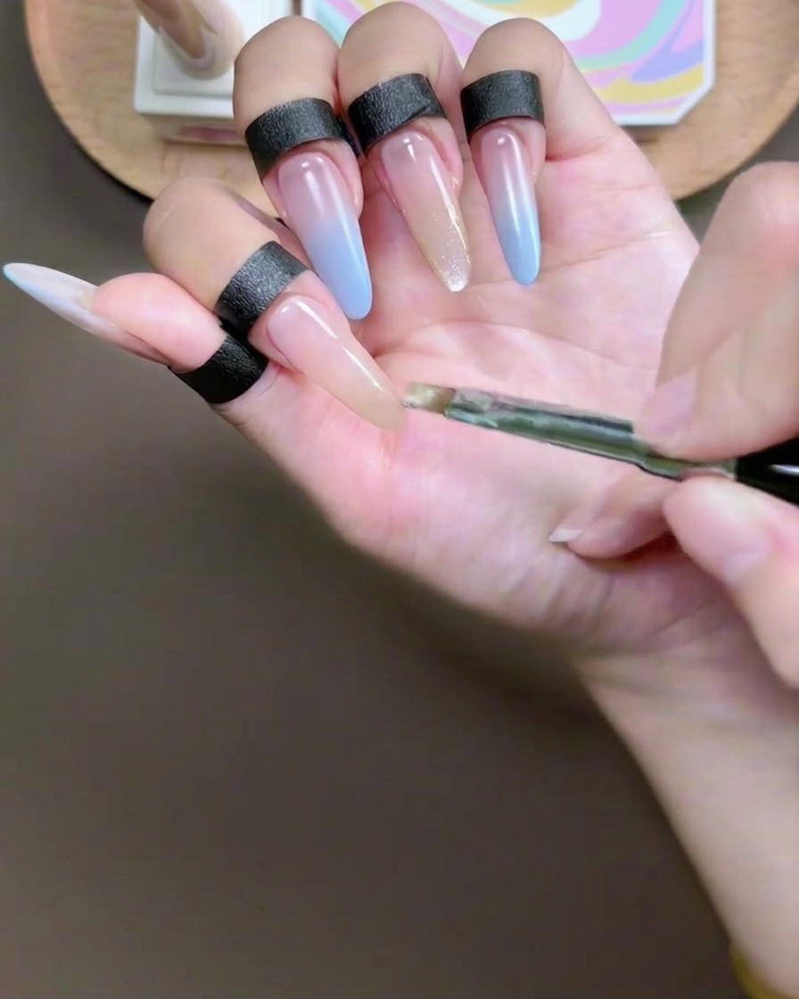 A gel brush applying a pigmented champagne cat-eye gel to the tip of an index fingernail.
