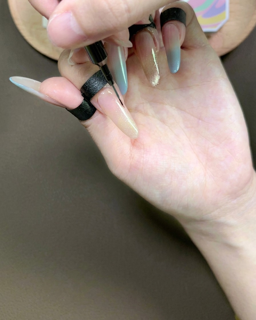 A fine liner brush gently dragging through the cat-eye gel on the index finger to create a smooth, tapered gradient.