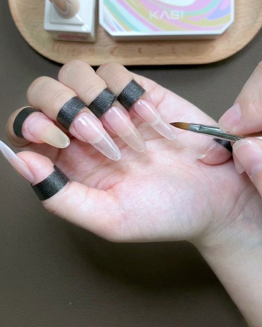A brush applying a clear, viscous builder gel over the entire surface of the index fingernail for encapsulation.