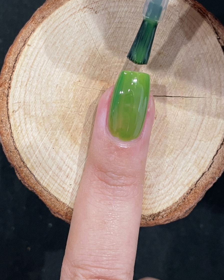 A brush meticulously applying green gel polish near the cuticle of a fingernail.