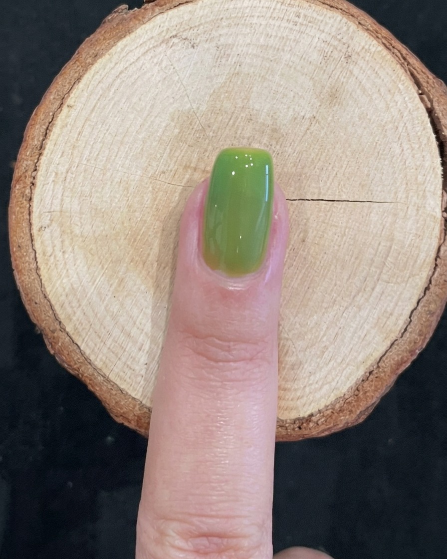 A clean, glossy, translucent green cured nail on a wooden surface.