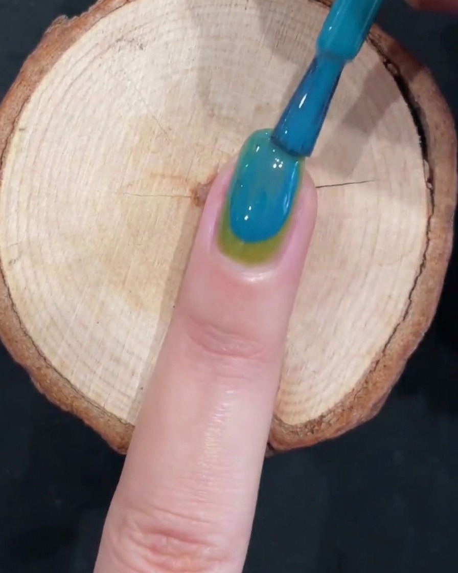 A brush creating a smooth gradient effect on a two-toned green and blue nail.