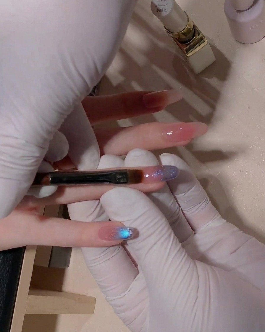 A close-up shot showing a flat gel brush gently blending the transition area of blue cat-eye gel on the nail surface.