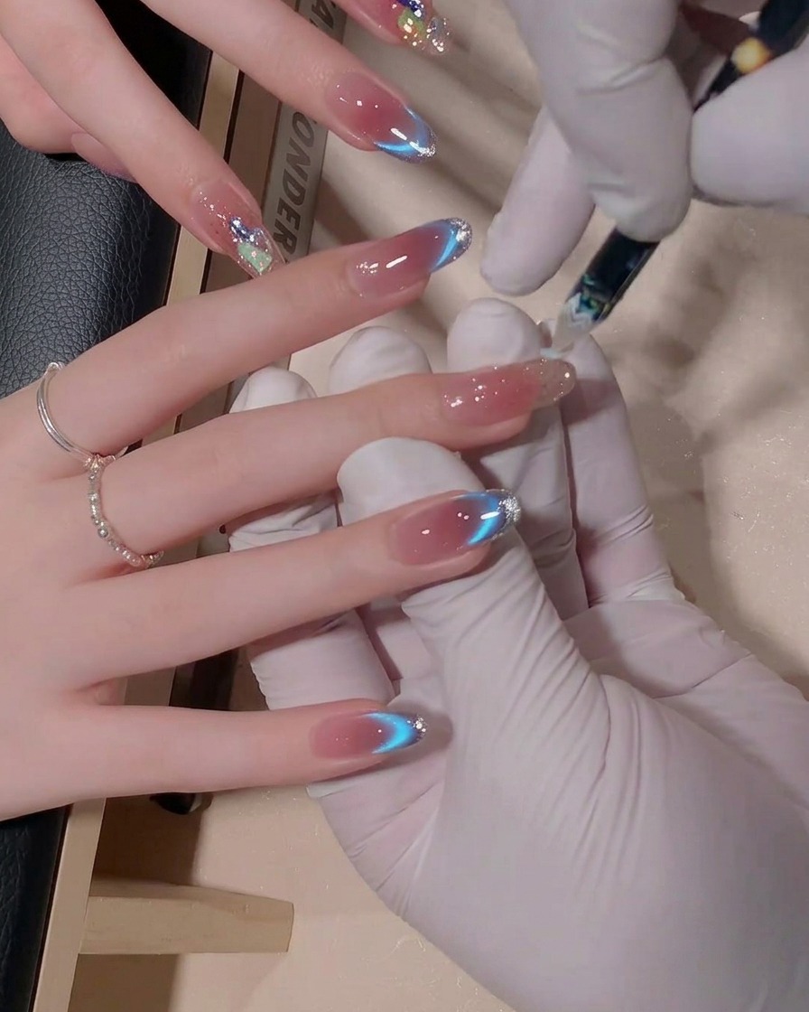 A close-up view of a nail brush being used to blend blue-toned gel polish on a fingernail to create a soft, seamless gradient effect.
