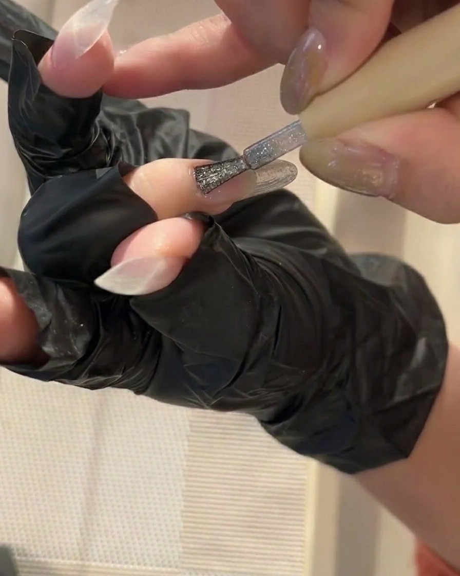 A small brush applying a thin layer of clear gel base coat onto a clean nail.