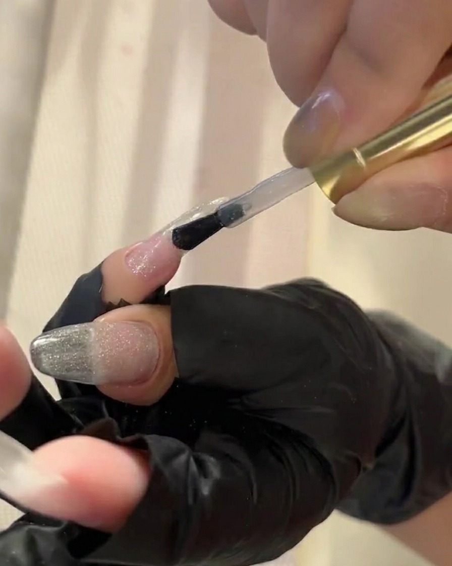 A brush applying a clear top coat to a nail, preparing it for pigment powder application.