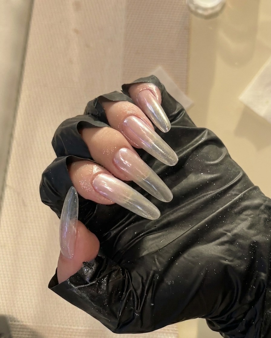 A close-up view of long, clear, almond-shaped nails being refined along the side edges with a professional nail file.