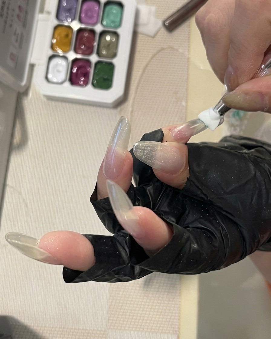 A close-up of a nail brush blending a soft mint-green gel color onto the surface of a long, structured nail to create a delicate gradient.
