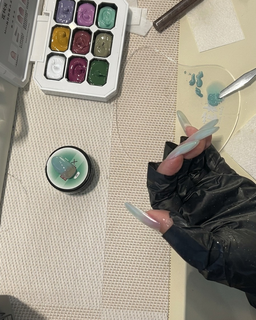 A nail brush applying a final, glossy top coat to a long nail featuring a soft mint-green gradient design.
