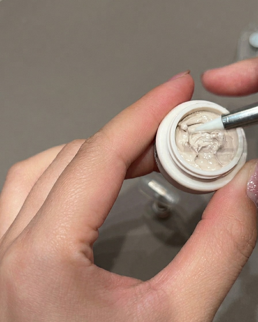 A close-up view of a precision liner brush applying small brown dots onto a gel-painted nail.