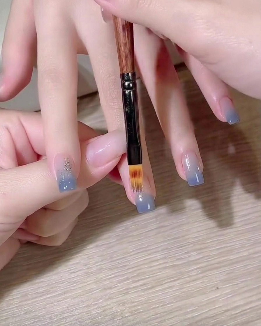 A flat gel brush blending a blue color gradient on a nail.