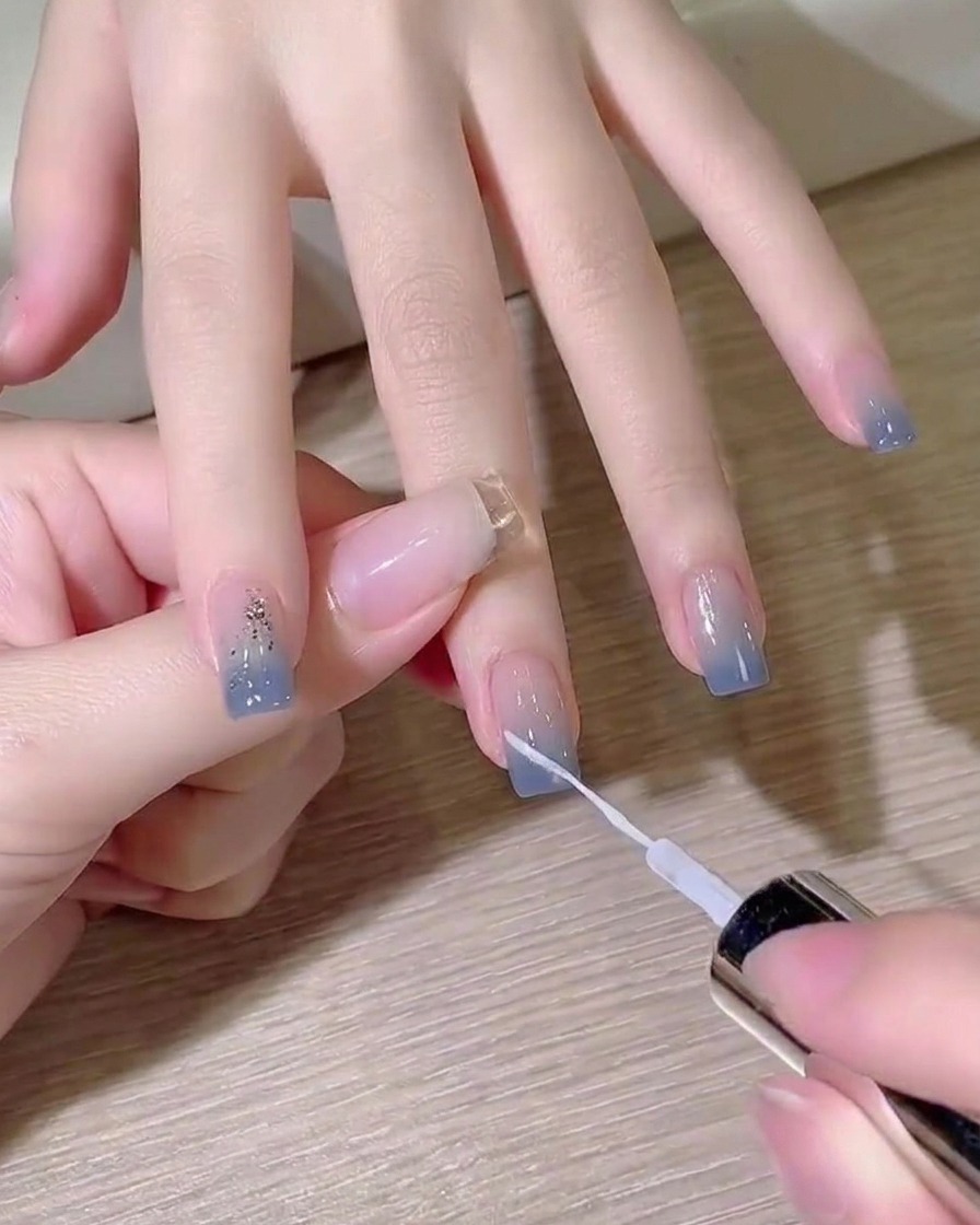 A fine liner brush painting a crisp diagonal white line over a blue ombre nail.