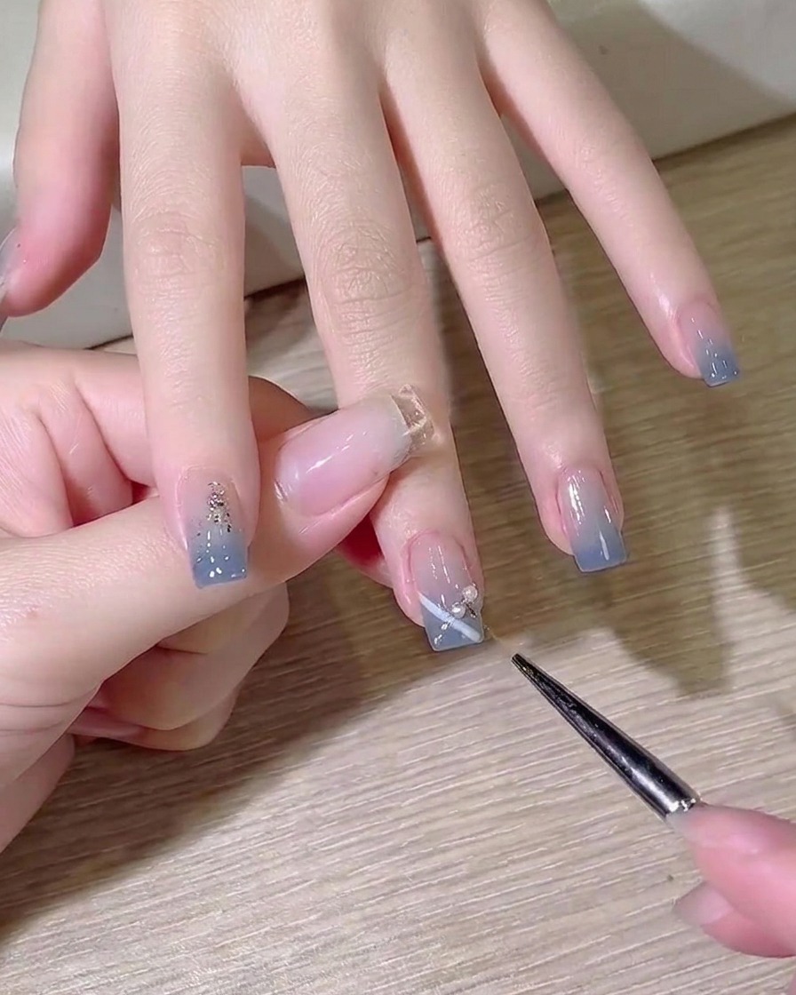 A detail brush applying a small drop of clear builder gel onto the nail surface as an adhesive.