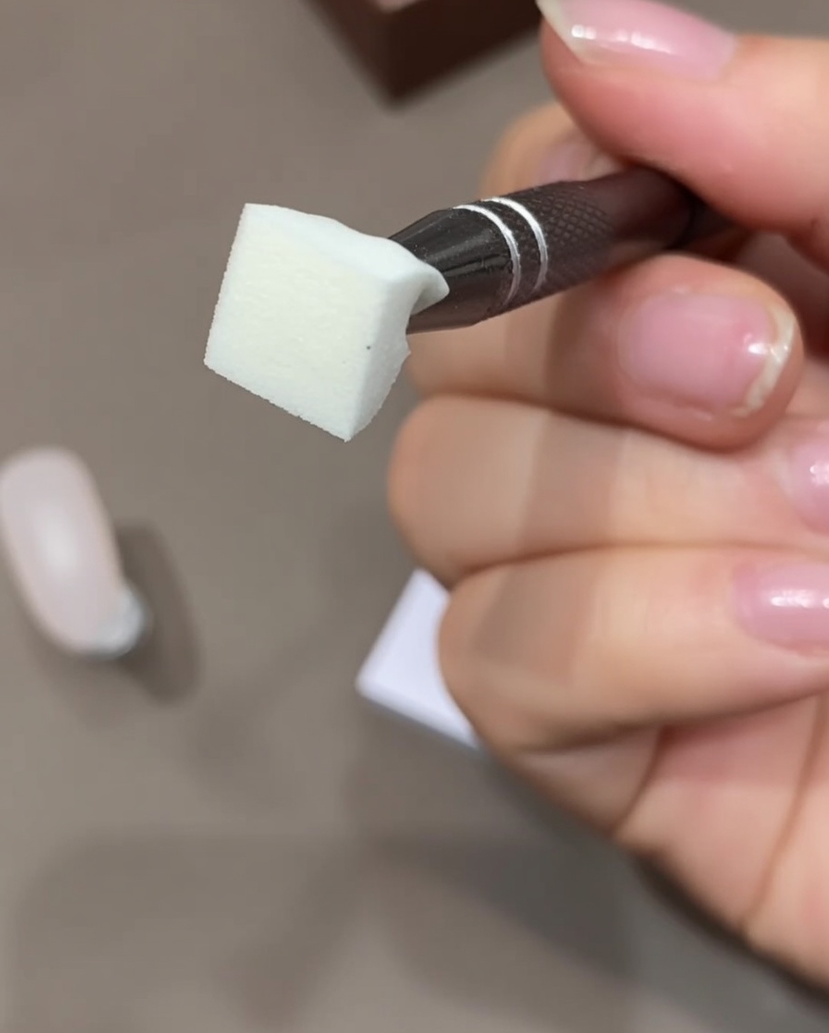 A close-up view of a hand holding a makeup sponge and using tape to remove surface dust.