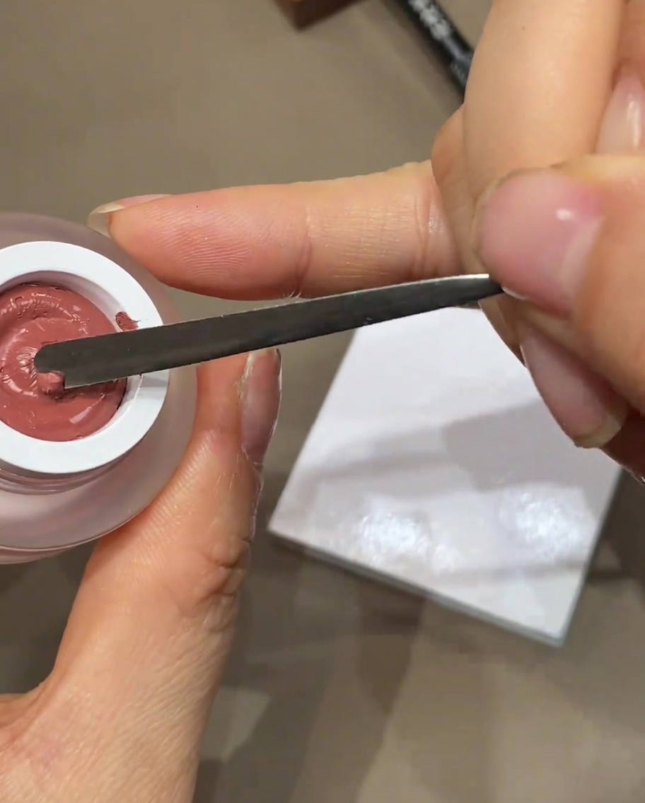A metal spatula dispensing a small dollop of colored gel polish onto a white palette.