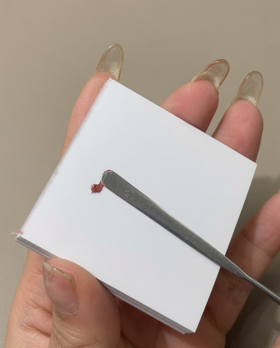 A metal spatula smoothing out a line of colored gel polish on a palette surface.
