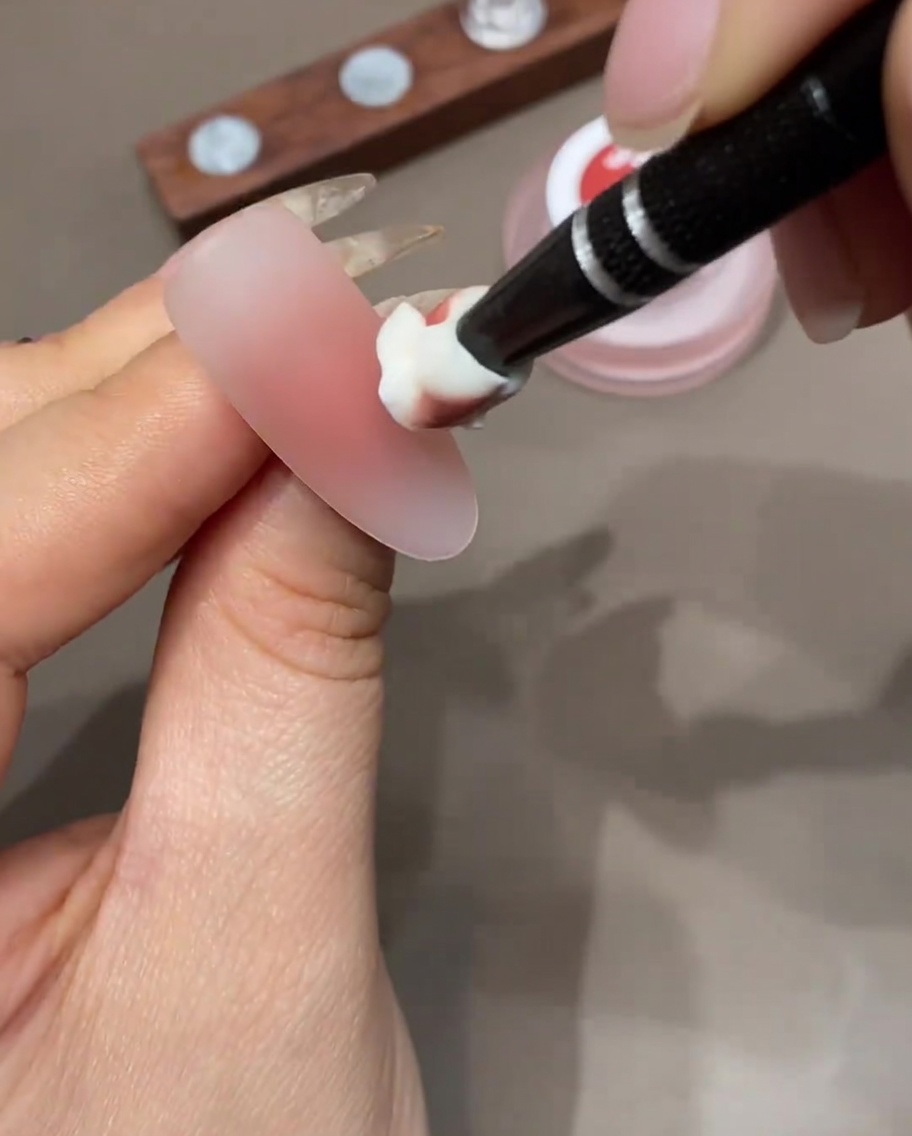 A makeup sponge applying a layer of colored gel to the tip of a nail to build an ombre gradient.