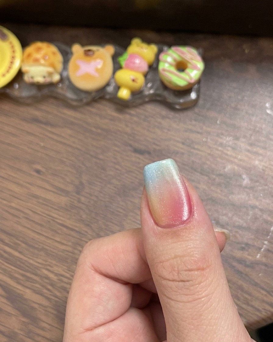 A magnetic tool held near the side of a nail coated in wet cat-eye gel to create a sharp light reflection.