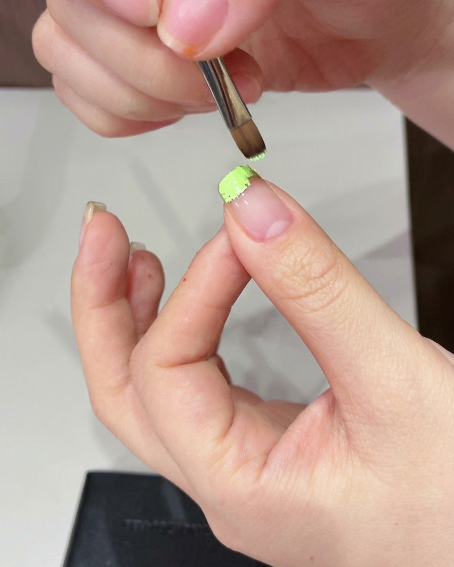 A sponge being used to dab and soften the green gel on the nail tip.