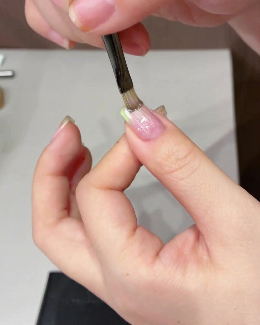 A cylindrical magnet being used to sweep back and forth on one side of the nail to create the cat eye effect.