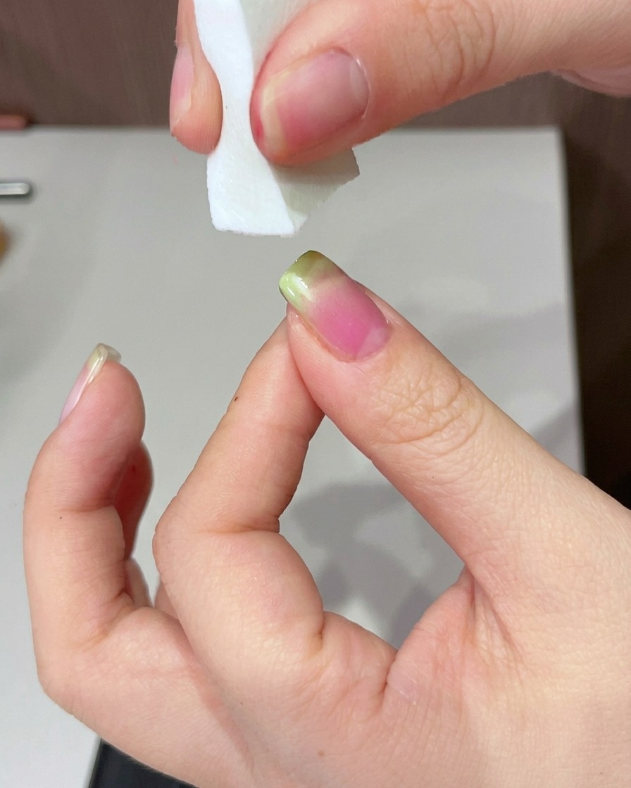 A hand positioned under a UV lamp to cure the green-tipped nail.