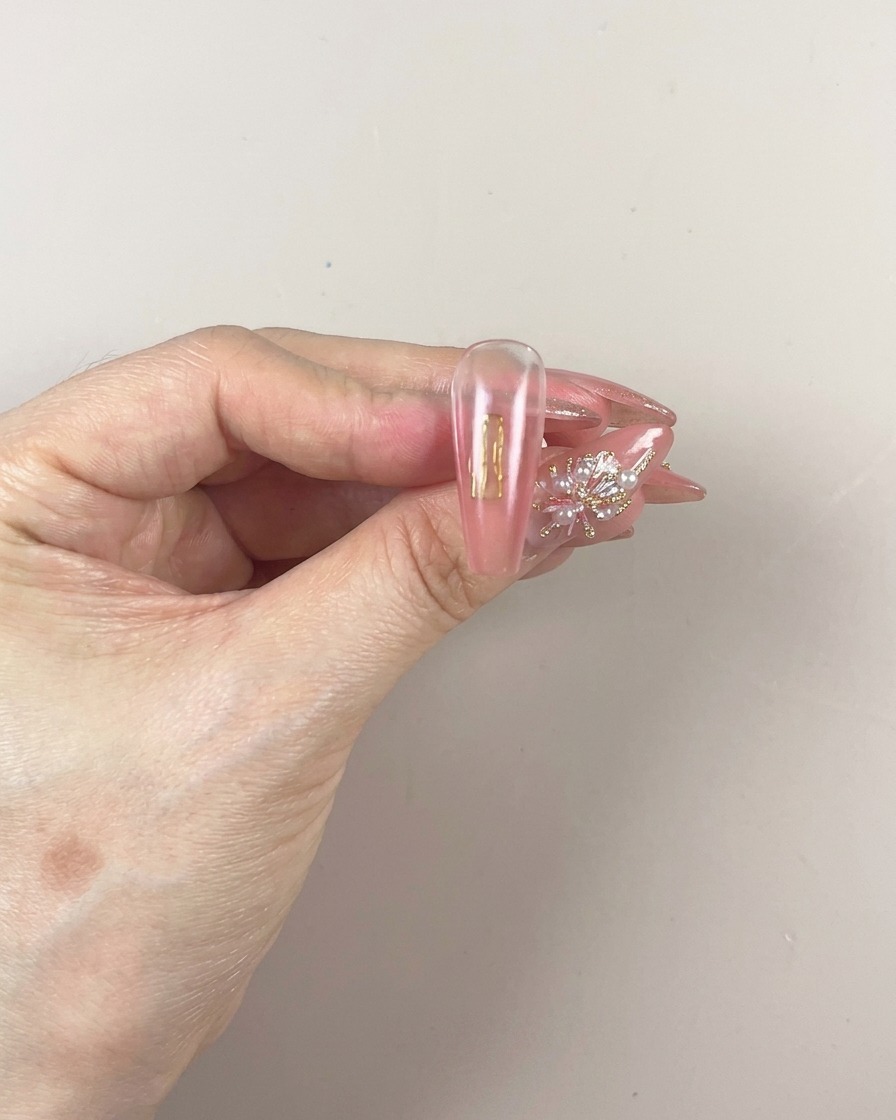 A brush applying a fresh layer of pigmented patting gel onto the lower portion of the nail.