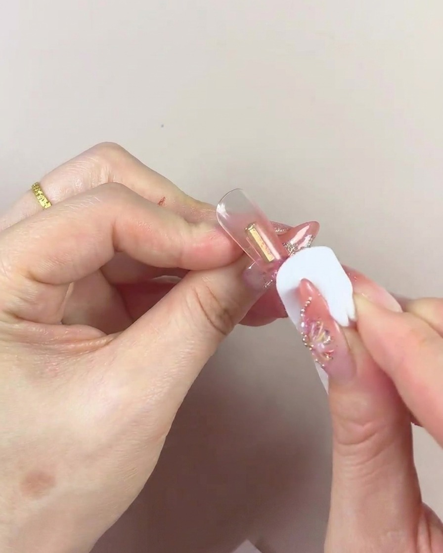 A close-up of a cosmetic sponge with a dark center being used to pat gel onto a nail tip.