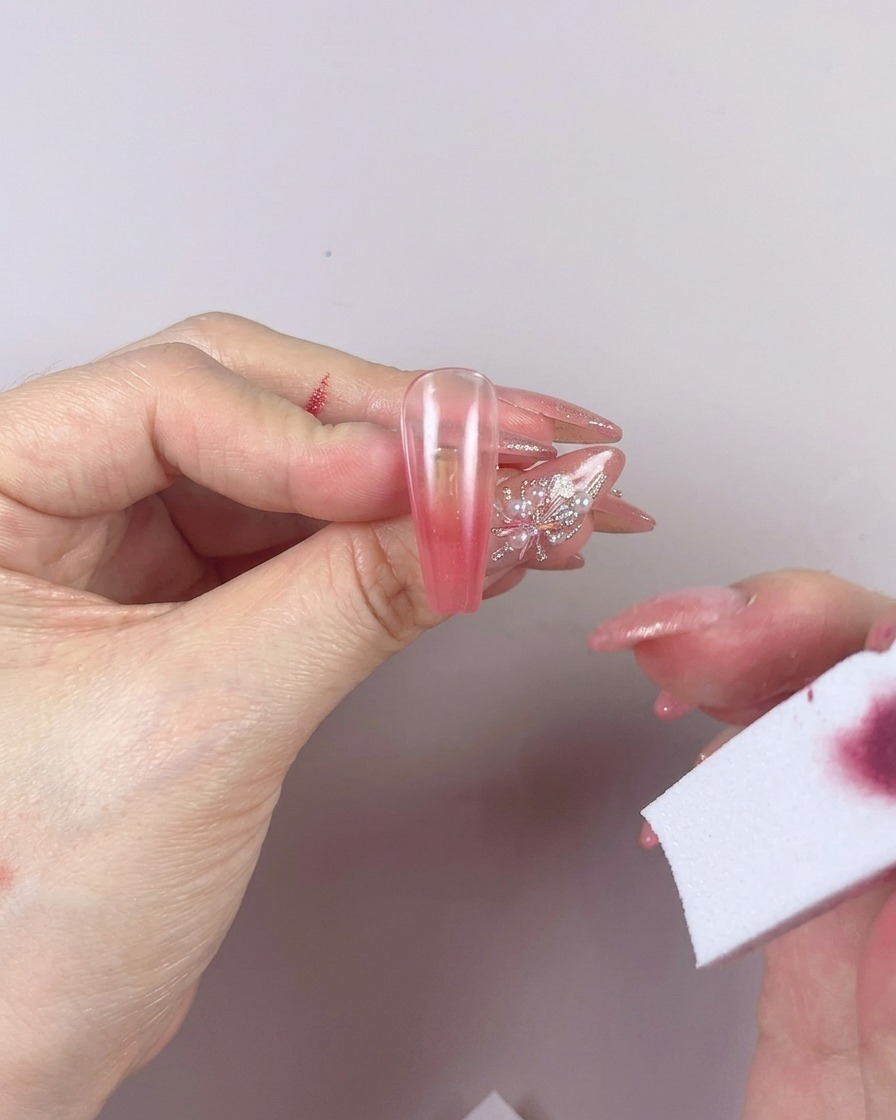 A sponge being used to blend the gel color on a nail with horizontal left-to-right motions.