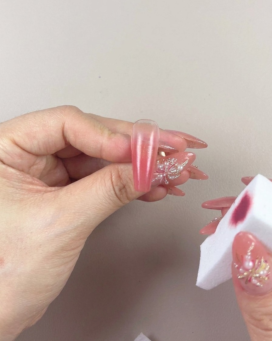 A close-up of a hand using a makeup sponge to gently pat and blend the gradient on a nail.