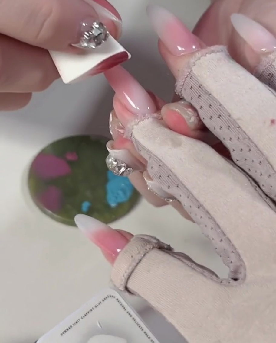 A close-up of a sponge pressing onto blue and pink gel polish blocks on a mixing palette.