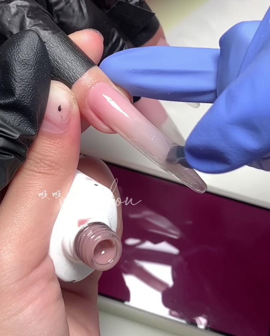 A close-up of a brush applying a bright magenta gel to the outer half of the nail.