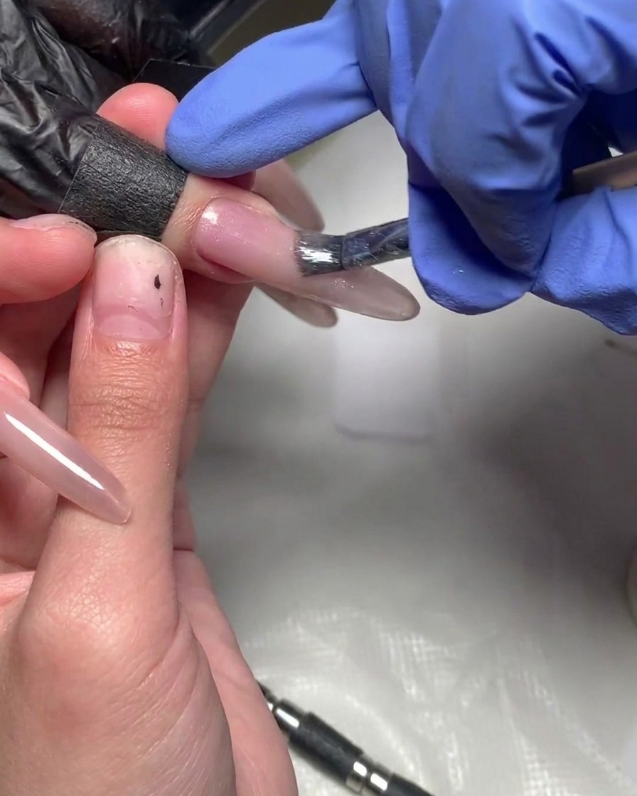 A brush applying a fresh layer of magenta gel to the very tip of the nail to increase color intensity.
