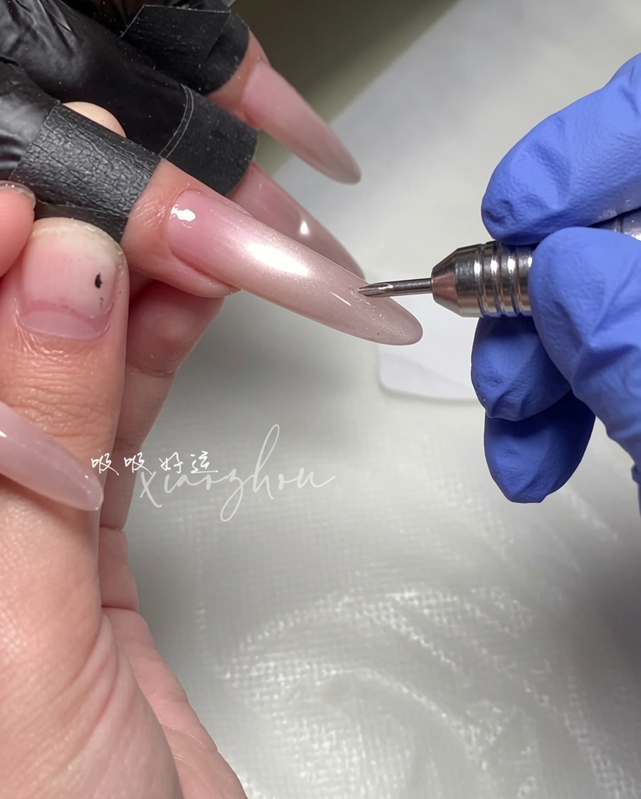 A hand holding a magnetic wand tool over a long, almond-shaped nail coated in wet magenta cat-eye gel polish.